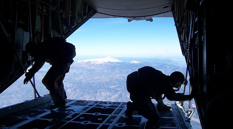 two people in military fatigues inside an open cargo area of an airplane