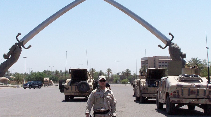 man in military fatigues standing in front of military vehicles and a large arch